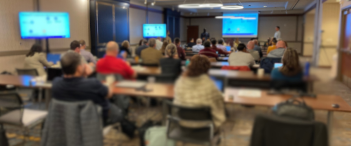 People in a large room watching a presentation.